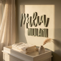 Personalized 3D wooden wall art reading 'Malia MILILANI' in a warm, neutral-toned nursery setting above a changing table with folded cream towels and a small vase.