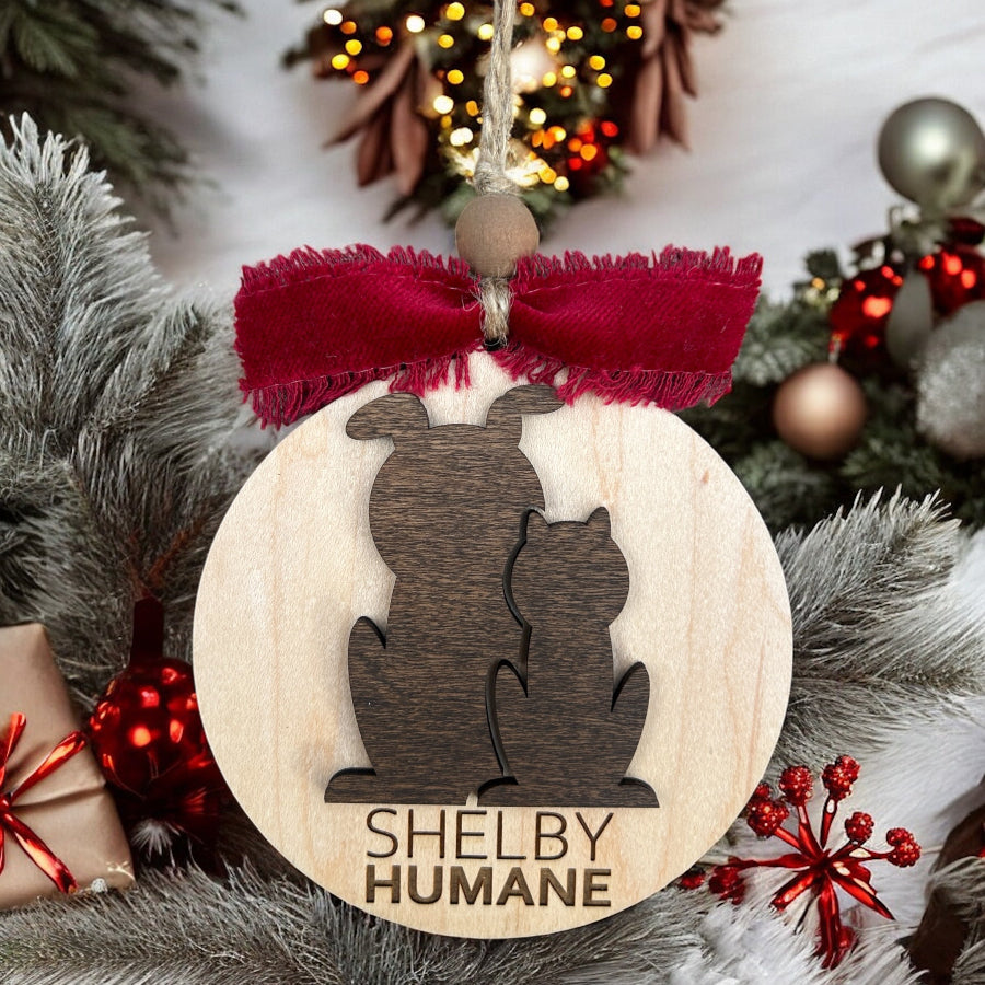 Wooden ornament with cat and dog silhouette and 'Shelby Humane' text, surrounded by Christmas decorations.