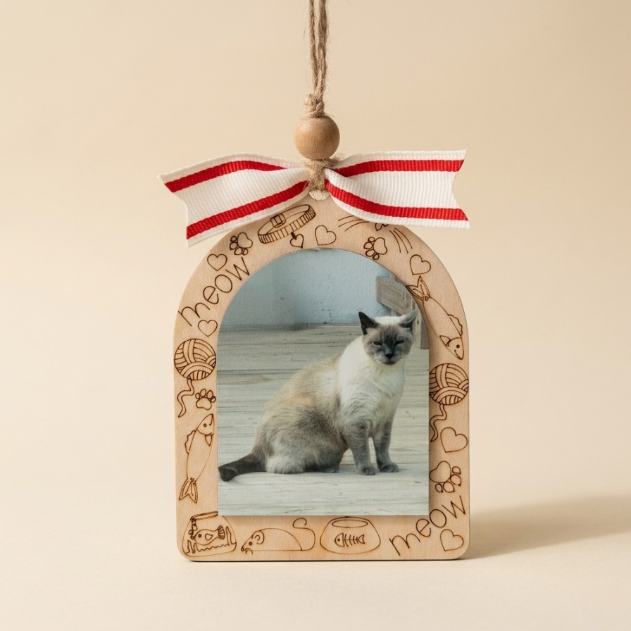 A wooden arched hanging ornament with a photo slot displaying a cat, decorated with engraved cat illustrations and the word 'meow', topped with a red and white striped ribbon bow and a wooden bead.