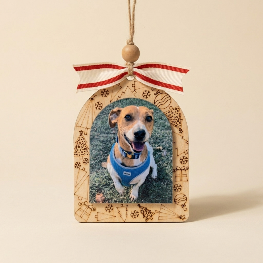 A wooden arched ornament featuring a printed photo of a dog wearing a blue harness, hanging from a red and white striped ribbon with a wooden bead.