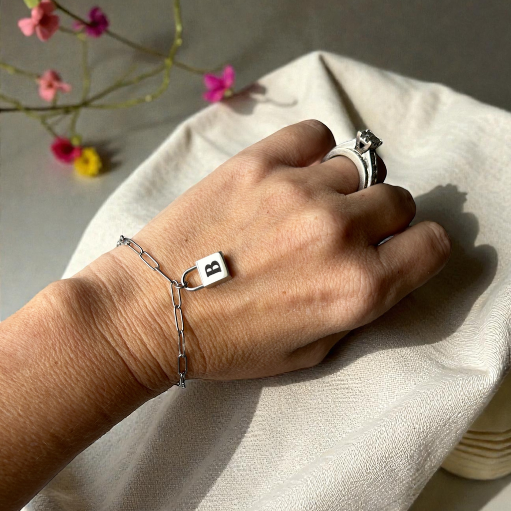 Hand wearing a silver lock bracelet engraved with a B.