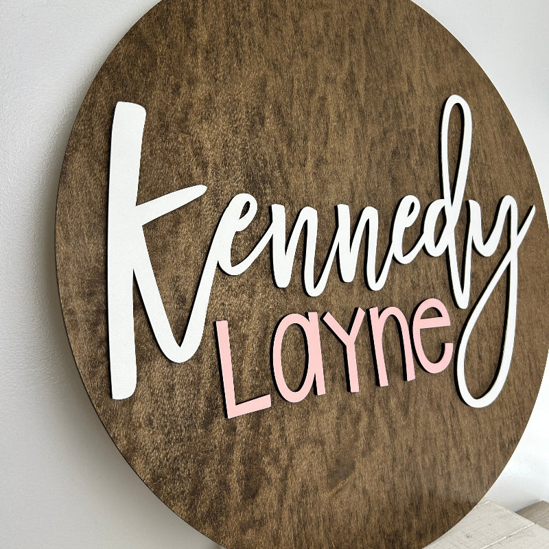 Dark wook round backer with the baby name cut out and painted in the colors that match the baby's nursery.